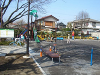 入口から入って右側から見た園内左に複合遊具、右側にブランコ、手前に鉄棒などの遊具が設置されている園内の写真