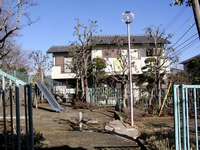 住宅に隣接し周囲に樹木があり、すべり台が設置されている小野並木公園を入口から撮影した写真