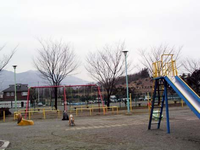 近くに木が半分伐採された山があり、園内にはブランコや鉄棒、すべり台などの遊具が設置されている、まつかげ台山の手公園の写真