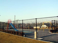 高さのある黒色の柵で囲まれた園内左奥に鉄棒、右側に黄色のブランコ、左手前にすべり台、右手前に水飲み場が設置されている北ヶ谷西公園の写真