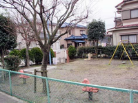 住宅街の一角にある緑色のフェンス内には植木や樹木が点在していて、ブランコや2つのスプリング遊具が設置されている王子原公園の写真