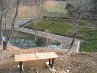 山を切り開いて造られた湧水池を望む高台に2人掛けのベンチが設置されている写真
