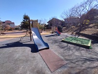 大型、小型すべり台、砂場のある日だまり公園の遊具広場の写真