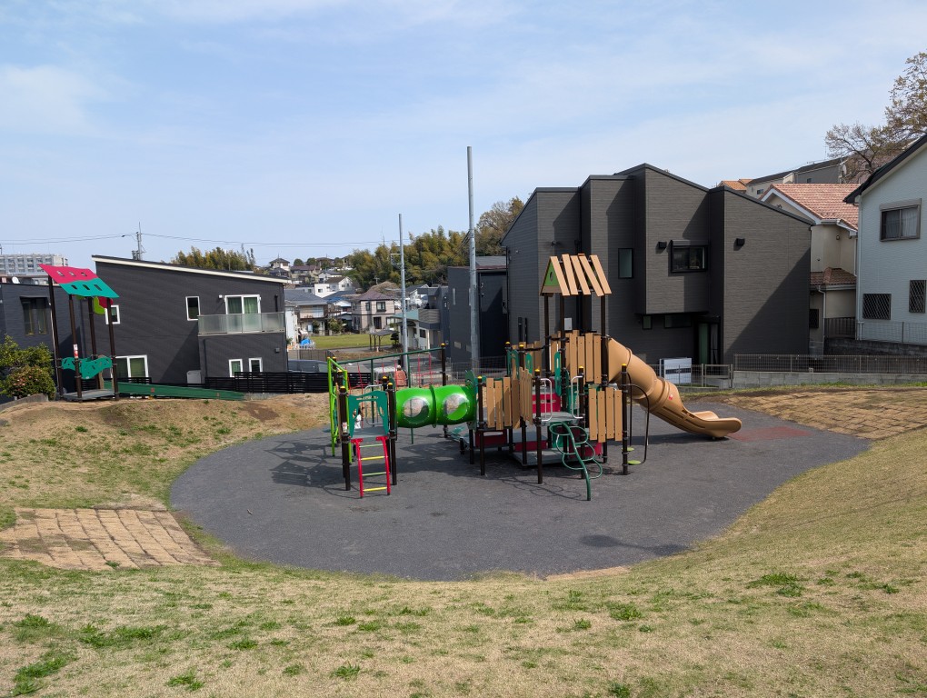 小高い丘を見上げると2つの遊具が設置されています。遊具を挟んで手前と奥に木製の見晴台があり、頂上付近に大きな木と植木が植えられているつつじ台公園の写真