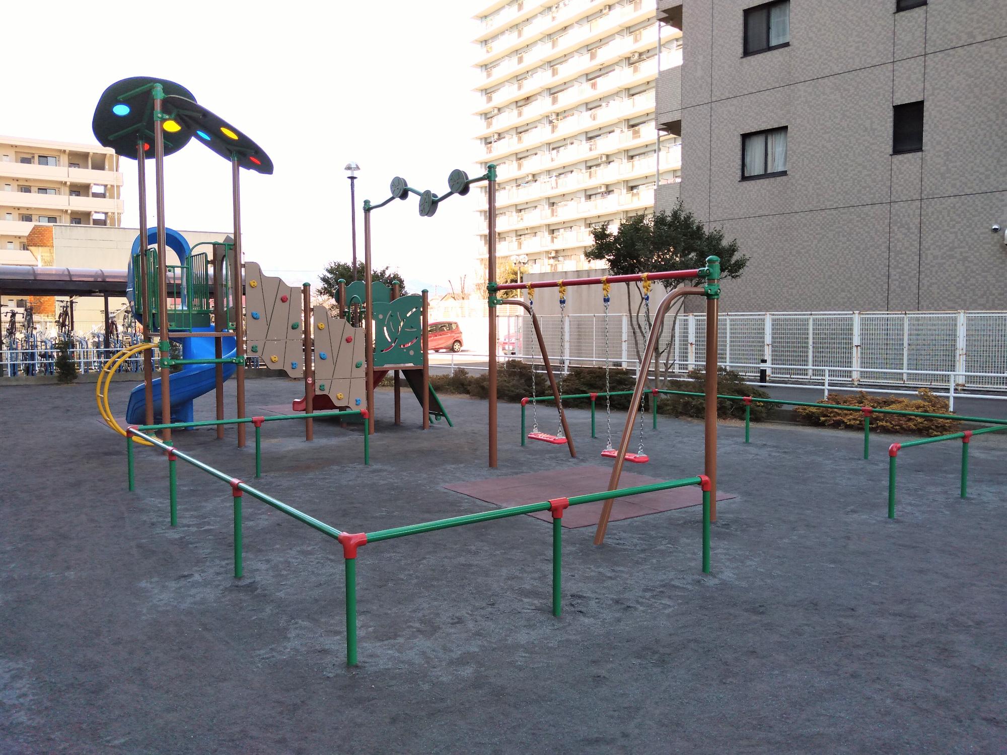 周囲には植木が植えられており、砂場に続くすべり台や上から吊るされたタイヤの遊具などが設置されている妻田東公園の写真