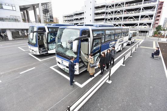 駐車場に停車している2台のバスの手前のバスに乗ろうとしている乗客をバス会社の男性が誘導している写真