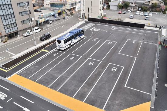 バスが9台駐車できるように道路に番号が書いてある駐車場に1台のバスが停車しているところを上空から写した写真