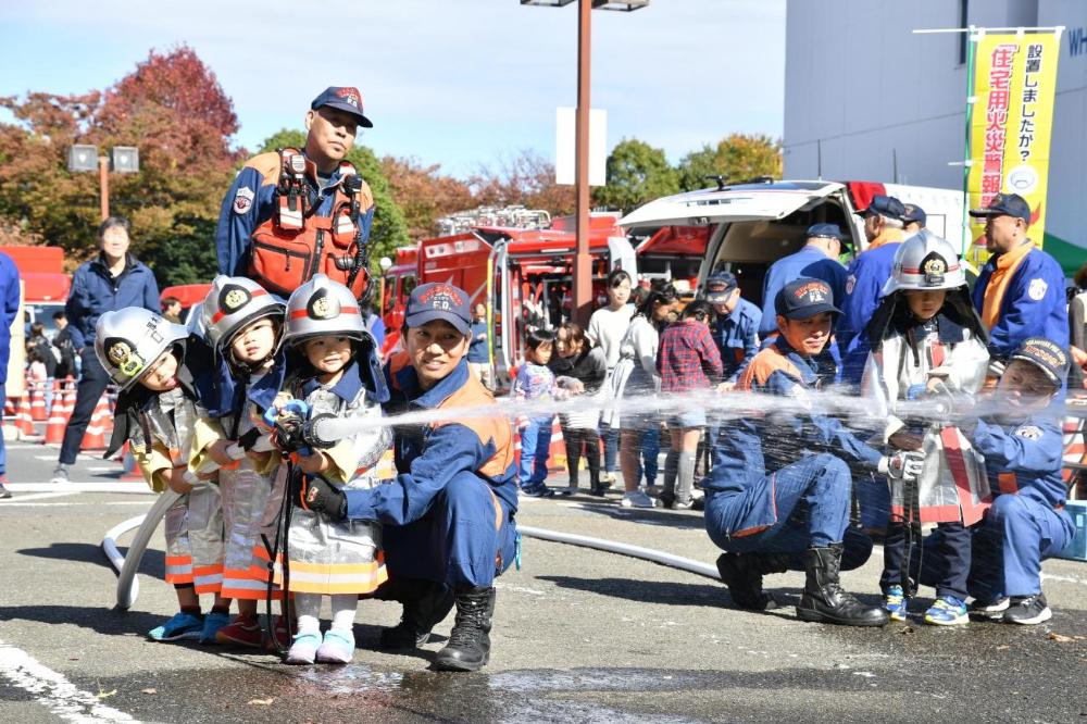 消防服を着用し消防用ホースをしっかり持ちながら、放水体験を楽しむ子供達の写真