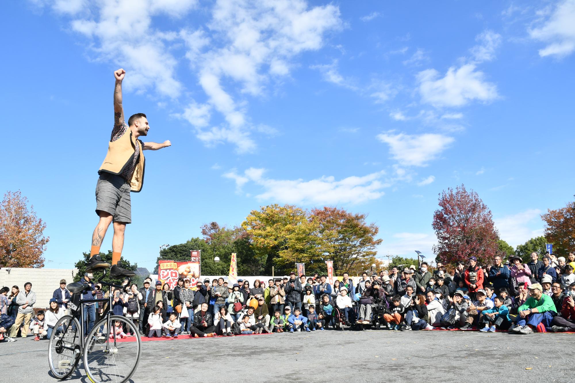 青空の下、厚木中央公園でのアクロバティックな曲乗り自転車と引き込まれる観客の写真