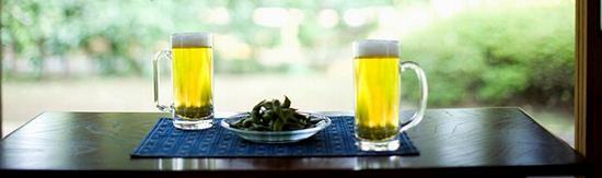 テーブルの上にジョッキに入ったビール2つと皿に盛られた枝豆の写真