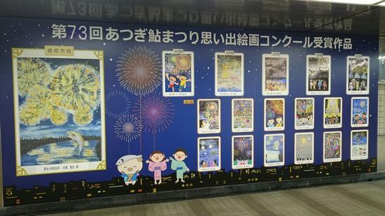 壁一面に貼られた大きなポスターに、思い出絵画コンクールの作品と、花火のイラストと男女とあゆコロちゃんのイラストが描かれている写真