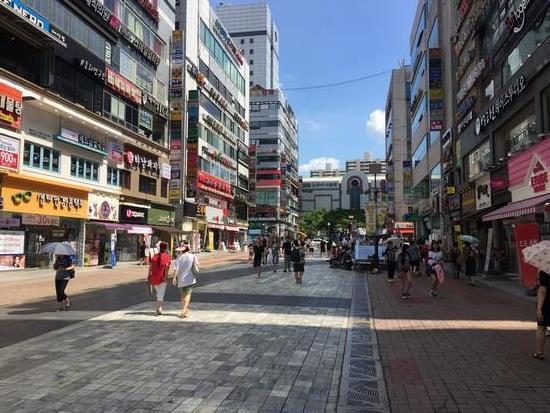 カラフルなショッピングビルが並んだ軍浦（くんぽ）市のメインストリートを人々が歩いている写真