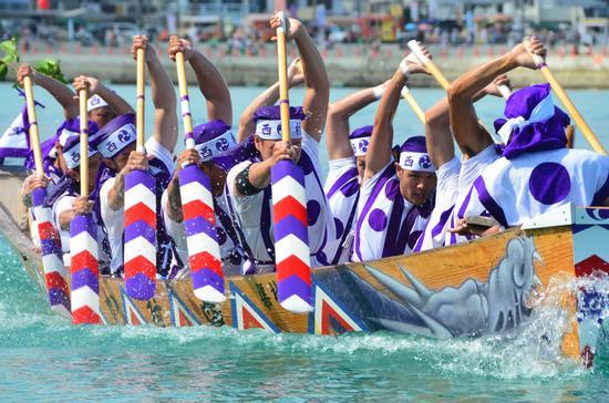 民族衣装のようなものを着た男性達が1艘のボートに10人乗りオールでボートを漕いでいる写真