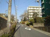 通り沿いの右側に白い建物の集合住宅が立ち並んでいる住宅地区の写真