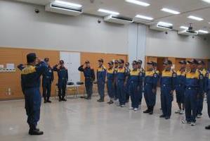 前に立った隊員と左側に並んでいる隊員が敬礼をしており、他の隊員が2列に整列している写真