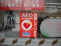 全体が目立つ赤色で、白文字で「AED 設置しています。」と書かれたシールが窓に貼られている写真
