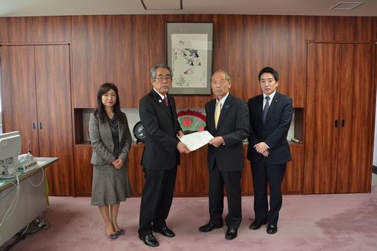 越智一久議長へ答申書を手渡す沼田幸一委員長、左端にスーツ姿の女性と右端に男性がたっている写真