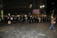夜の駅前でたくさんの議員の人達が並びチラシを配っている写真