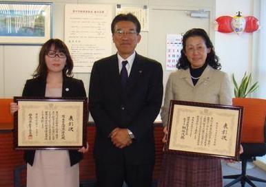平井教育長を中央に、與安栄養士と須藤清水小学校長が額に入った表彰状を持って記念撮影している写真
