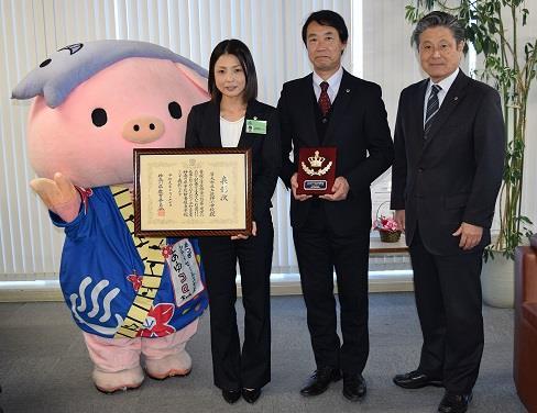 左から法被を着た豚のキャラクター、額に入った表彰状を持つ神崎栄養士、盾を持つ大谷 上荻野小学校長、曽田教育長が記念撮影をしている写真