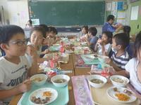 教室で生徒たちが向かい合って笑顔で給食を食べている写真