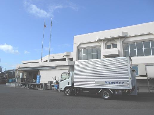 建物の前に学校給食センターの配送者が前に停まっており、天井が高く壁が白色の南部学校給食センター外観の写真