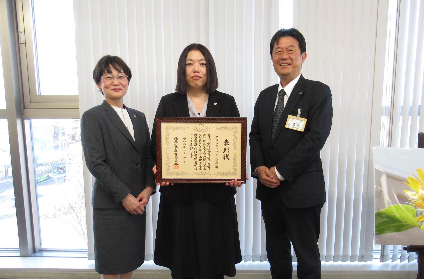 左から、武上依知小学校長、賞状を持つ寶地戸栄養士、佐後教育長が記念撮影をしている写真
