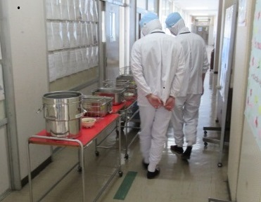 配膳しおわった食缶を見る調理員