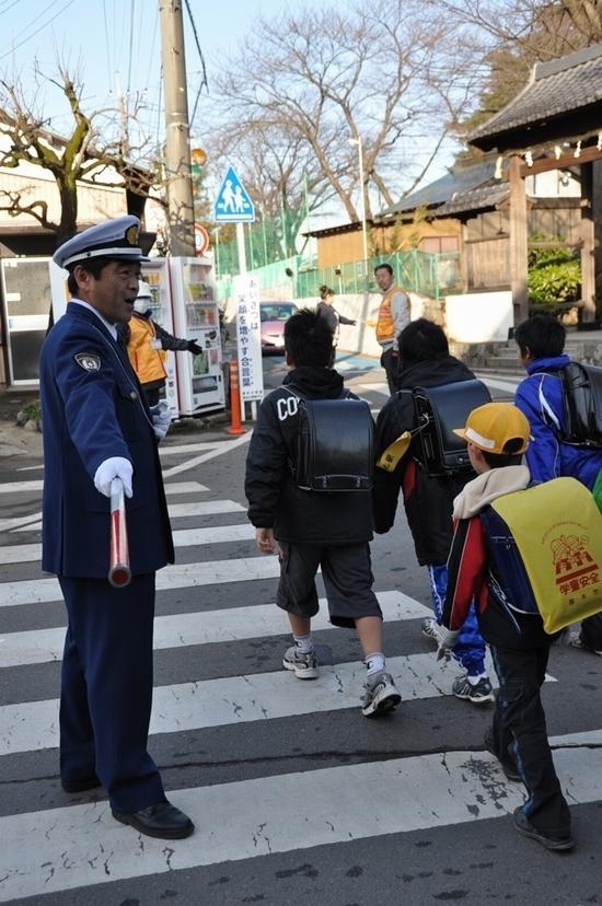 警察官が横断歩道に立ち、ランドセルを背負っている子供達を横断させている写真