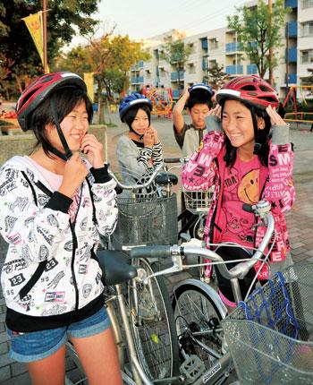 自転車に乗る前にヘルメットを被っている4名の生徒の写真