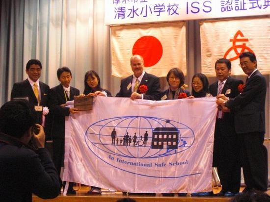 インターナショナルセーフスクール認証旗を8人で持って記念写真