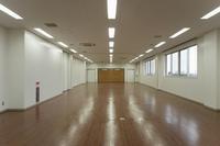 床が茶色で壁が白い奥行きのある広い集会室の写真