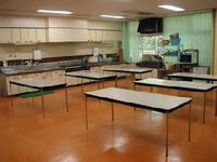 真ん中にテーブルが6台、周りに流し台やオーブンレンジが置いてある実習室の写真