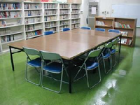 壁際に本棚が設置され、中央に椅子とテーブルが設置されている図書室の写真