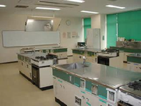前方の壁にホワイトボードがあり、調理台が置かれてある調理実習室の写真