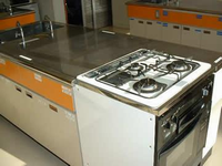 3口のガスコンロが設置された調理台が置かれている調理室の写真