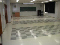 前方の壁に黒板が設置され、床にチェスボードの柄が入っている集会室の写真