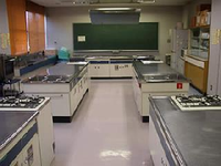 前方の壁に黒板が設置され5台の調理台が設置されている調理室の写真