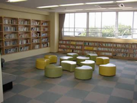 壁や、窓際に本棚が置かれ、中央に半円状の椅子が12個置いてある図書室の写真