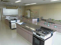 調理台が5台設置されており左奥の壁にはホワイトボードが設置されてある調理室の写真