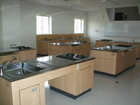 中央に調理台やガスコンロ、窓際に洗い場、壁にホワイトボードが設置されている調理室の写真