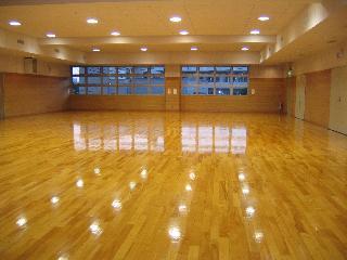 奥に窓ガラスがあって、天井の照明が床を反射させている広々とした第2体育室の室内の写真