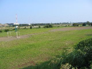 左奥に赤白の鉄塔があり、左手前にサッカーゴールのある河川敷にある旭町スポーツ広場の写真