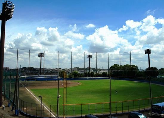 ナイター照明のある玉川野球場で青空の下、野球の試合が行われている写真
