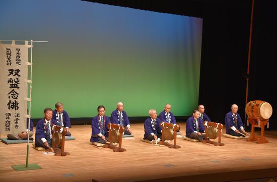 10名の紫色の法被を着た男性がステージ上の太鼓や双盤鉦の前に座っている写真