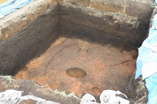 四角形に深く掘削した後に、中央に円形の跡が残っている発掘の跡の写真