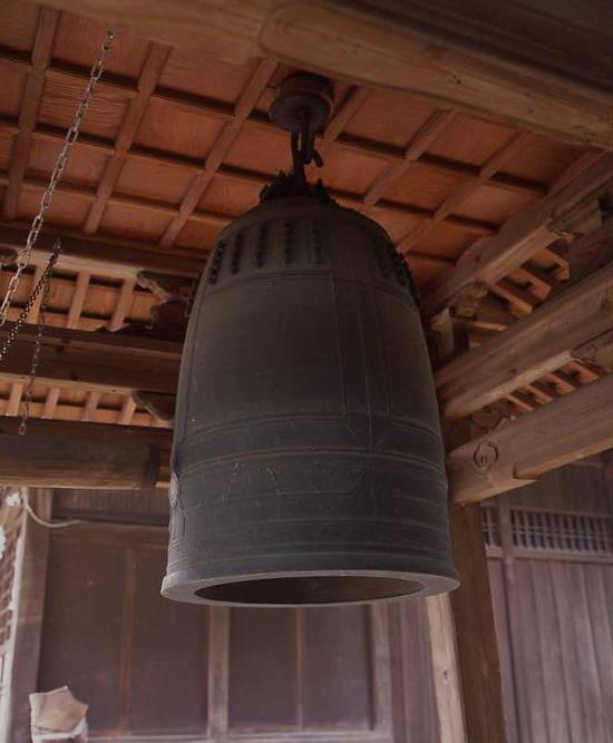 神社の境内の屋根に吊るされた大きな銅鐘の写真