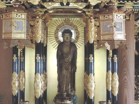 黒光りで上下に金箔の模様が施された左右の4本柱の中央に、放射状光背を負って立つ阿弥陀如来立像の写真
