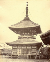 屋根が反って造られており、中央が円形になってくびれのある二重の塔の前に立っている人と左に待っている人が写っている白黒写真