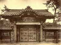 瓦屋根で中央が盛り上がっており、細かい装飾が施された門構えの屋敷の門を正面から撮影した白黒写真